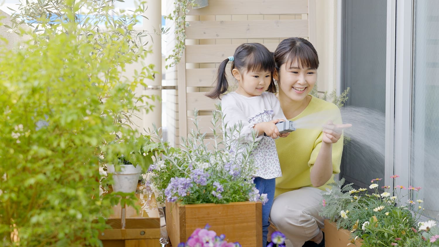 A mother and daughter watering flowers in a patio box.